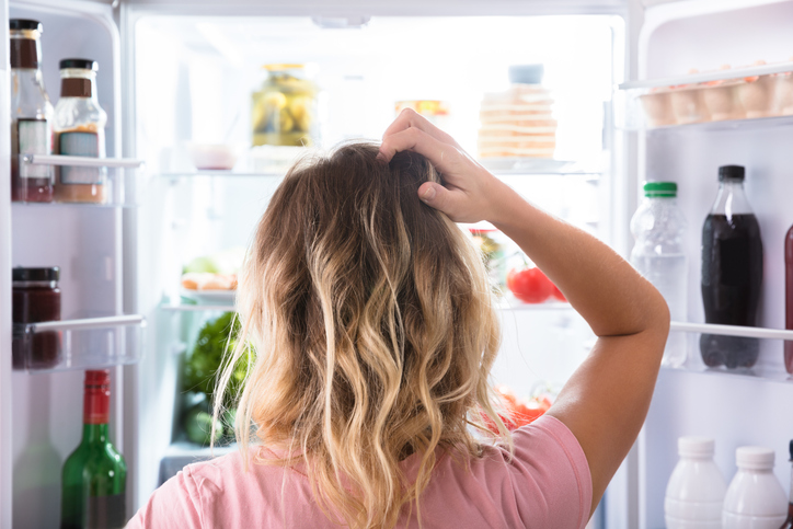 Une femme regarde dans le réfrigérateur d’un air perplexe 